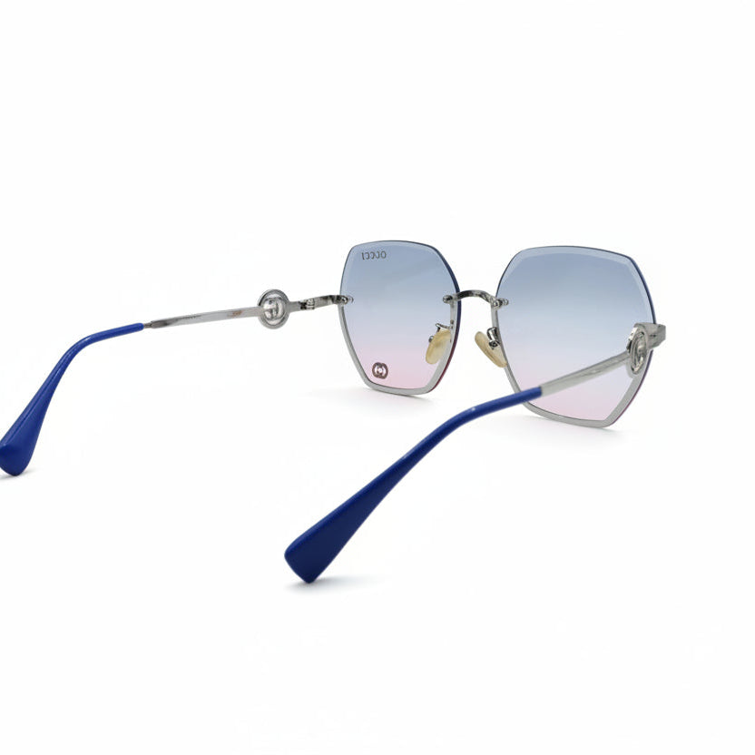 Oversized square sunglasses with a silver-tone metal frame, gradient blue-to-pink lenses, and blue temple tips, displayed on a white surface between two silver fabric panels.