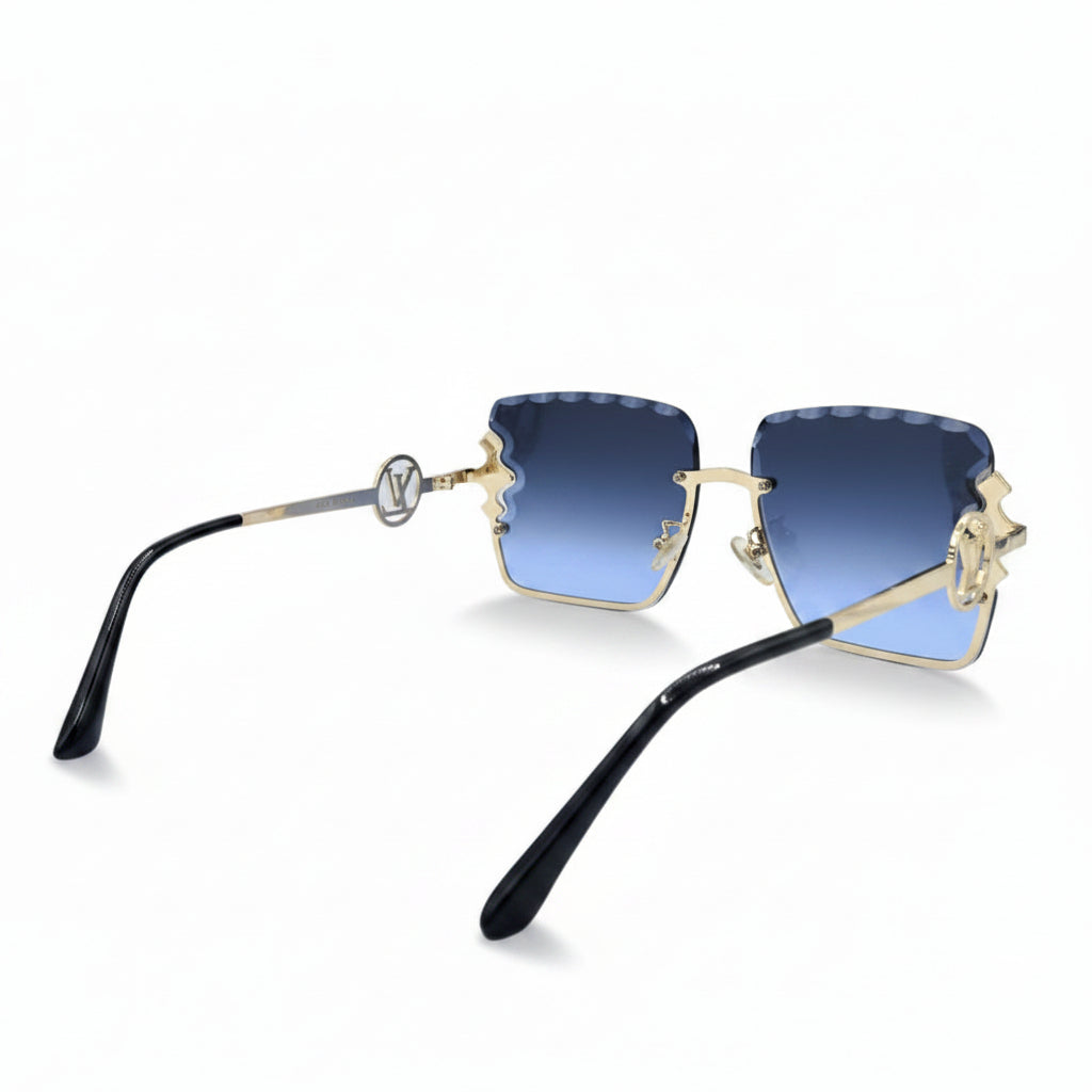 A pair of designer sunglasses with a gold-tone frame, blue gradient lenses, and a prominent interlocking LV logo on the temple, displayed on a white surface with textured silver props.