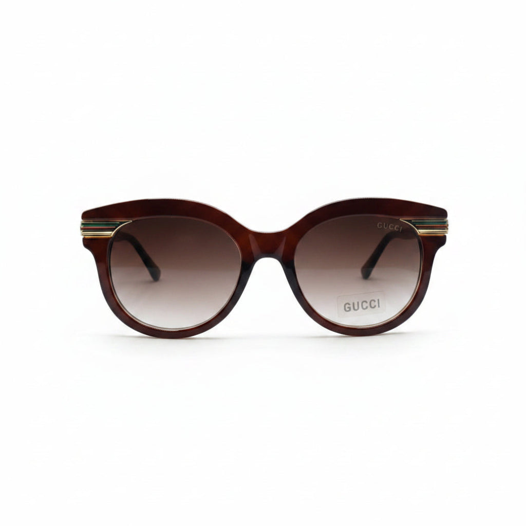 Gucci cat-eye sunglasses with a translucent dark brown frame and gradient brown lenses, featuring gold metal double stripes on the temples and the Gucci logo on the lens.