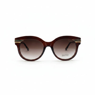 Gucci cat-eye sunglasses with a translucent dark brown frame and gradient brown lenses, featuring gold metal double stripes on the temples and the Gucci logo on the lens.