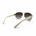 A pair of aviator-style sunglasses with cream-colored arms, gold metal frames, and brown gradient lenses, displayed on a white surface with a softbox background.