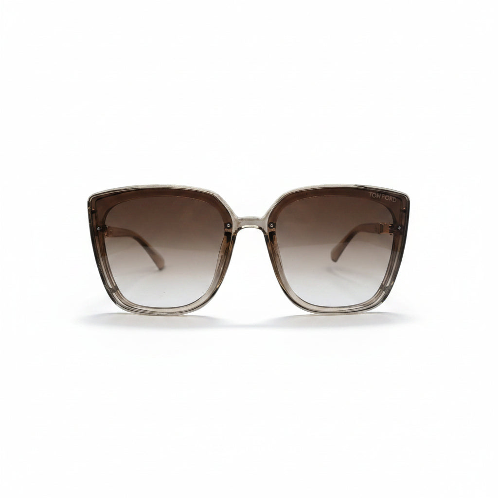 A pair of oversized square sunglasses with a translucent taupe-brown acetate frame and brown gradient lenses, displayed on a white surface with two textured silver props on either side.