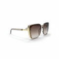 A pair of oversized square sunglasses with a gold metal frame and brown gradient lenses, displayed on a white surface between two textured black props.