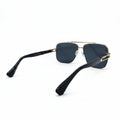 A pair of aviator-style sunglasses with dark blue lenses, a gold metal frame, and black temples, displayed on a white surface with a silver studio backdrop.