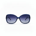 Oversized cat-eye sunglasses with a dark blue acetate frame and gradient purple lenses, displayed on a white surface between two silver studio reflectors.