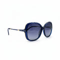 A pair of vintage-style cat-eye sunglasses with dark blue acetate frames and dark gray lenses, resting on a white surface between two silver reflective studio panels.