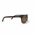 A pair of square-frame sunglasses with a dark brown acetate frame and brown-tinted lenses, displayed on a white surface with textured silver stands in the background.