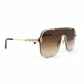 A pair of oversized square aviator-style sunglasses with a gold metal frame and gradient brown lenses, displayed on a white surface with a black textured backdrop visible on the sides.
