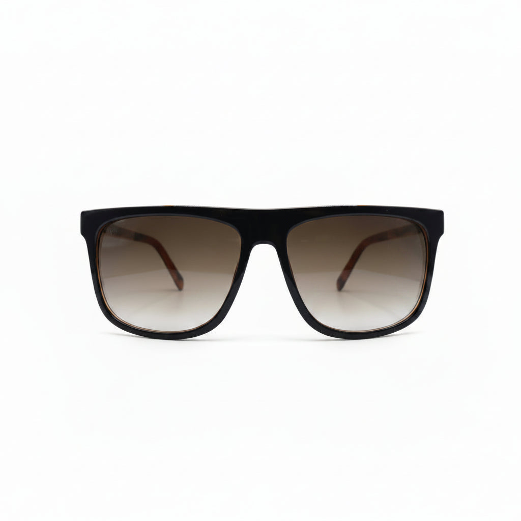 A pair of square-frame sunglasses with a thick black frame and brown gradient lenses, displayed on a white surface with two black fabric panels in the background.