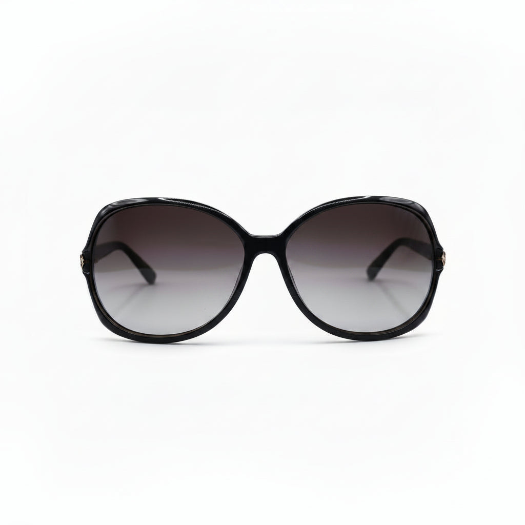Oversized sunglasses with a chunky black frame and gradient brown-tinted lenses, displayed on a white surface with a reflective silver pouch on each side.