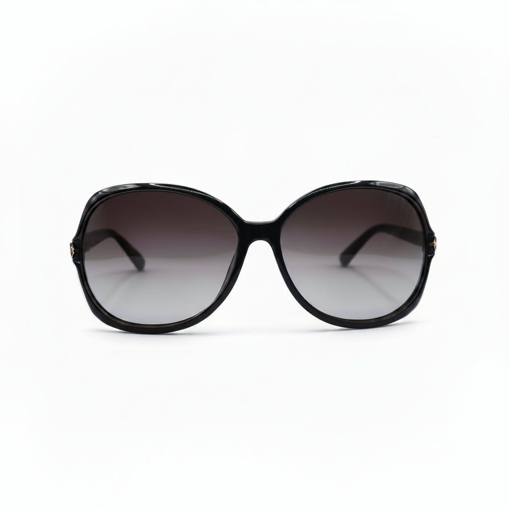 Oversized sunglasses with a chunky black frame and gradient brown-tinted lenses, displayed on a white surface with a reflective silver pouch on each side.