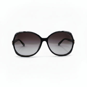 Oversized sunglasses with a chunky black frame and gradient brown-tinted lenses, displayed on a white surface with a reflective silver pouch on each side.
