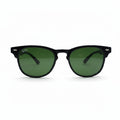 Black classic-style sunglasses with green lenses, featuring a visible Ray-Ban logo sticker on the lens, set against a white background with textured gray props on either side.