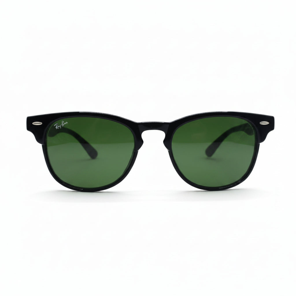 Black classic-style sunglasses with green lenses, featuring a visible Ray-Ban logo sticker on the lens, set against a white background with textured gray props on either side.