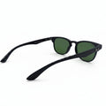 Black sunglasses with green lenses, displayed on a white surface with textured silver props on either side.