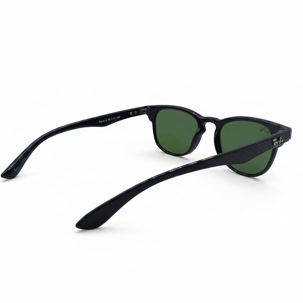 Black sunglasses with green lenses, displayed on a white surface with textured silver props on either side.