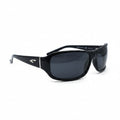 Black wrap-around sunglasses with dark lenses and a small silver logo on the temple, displayed on a white surface with reflective silver props in the background.
