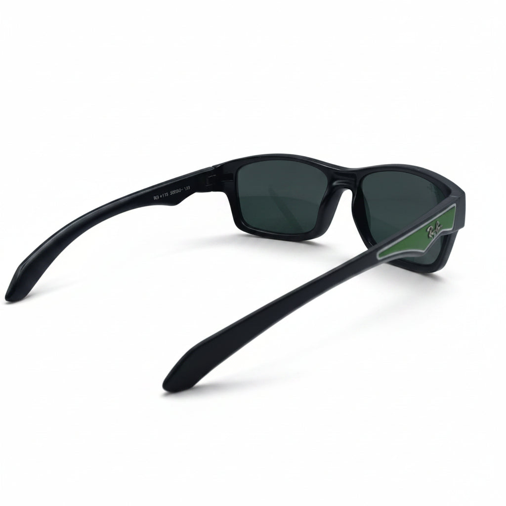Black wrap-around sunglasses with dark lenses and a green accent on the temple arm, displayed on a white surface between two textured silver panels.