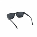 Black wrap-around sunglasses with dark lenses, displayed on a white surface with two textured black props on either side.