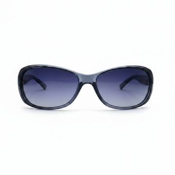 A pair of women's sunglasses with a dark gray translucent frame and gradient purple-blue lenses, displayed on a white surface with two textured gray props on either side.