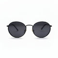 Round black sunglasses with dark lenses and a thin black metal frame, displayed on a white surface with two textured black bags on either side.