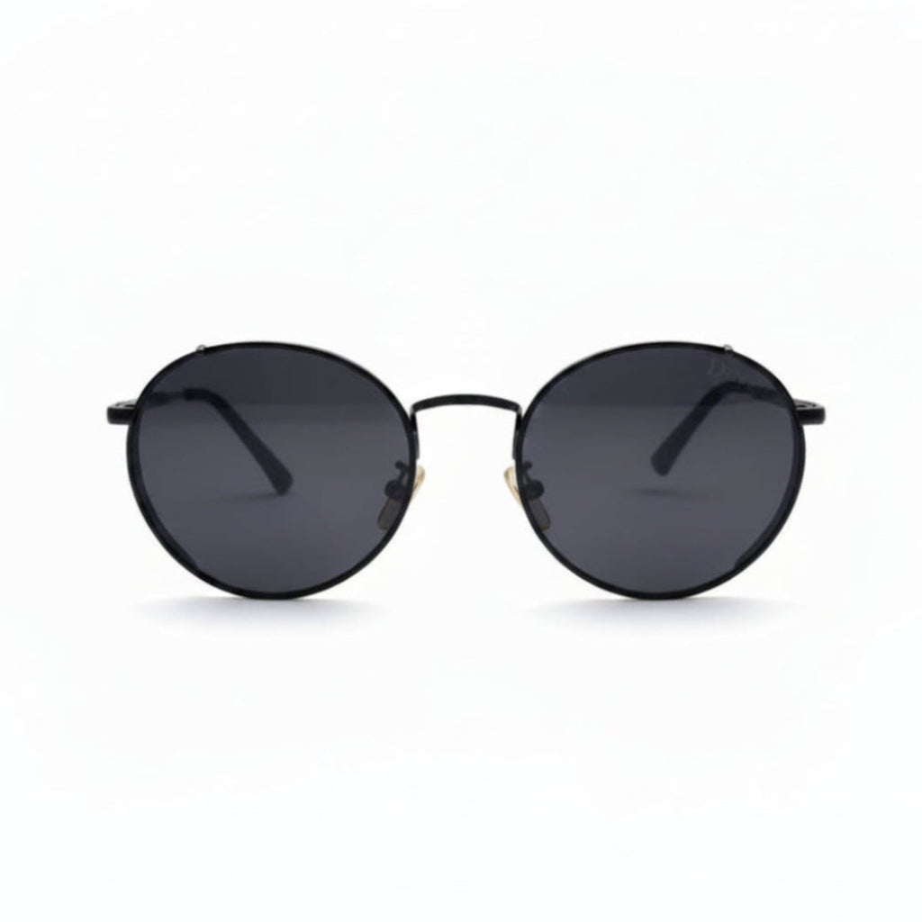 Round black sunglasses with dark lenses and a thin black metal frame, displayed on a white surface with two textured black bags on either side.