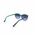 A pair of cat-eye sunglasses with translucent teal-blue frames and dark blue gradient lenses, resting on a white surface with a silver lightbox background visible on both sides.