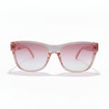 Pink cat-eye sunglasses with a translucent pink frame and pink gradient lenses, displayed on a white surface with black studio lights in the background.