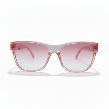 Pink cat-eye sunglasses with a translucent pink frame and pink gradient lenses, displayed on a white surface with black studio lights in the background.
