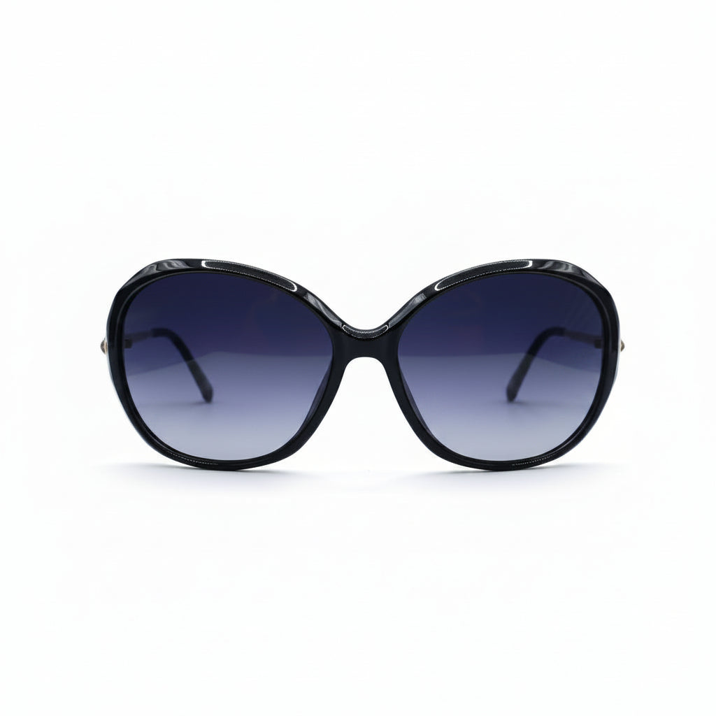 Oversized cat-eye sunglasses with a black frame and dark gradient lenses, displayed on a white surface with two silver studio reflectors in the background.