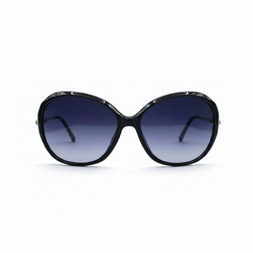 Oversized cat-eye sunglasses with a black frame and dark gradient lenses, displayed on a white surface with two silver studio reflectors in the background.