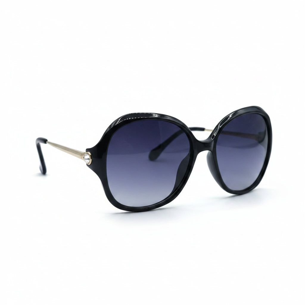 Oversized cat-eye sunglasses with a black frame and dark gradient lenses, displayed on a white surface with two silver studio reflectors in the background.