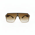 A pair of oversized shield-style sunglasses with a gradient brown lens and gold metal frames, displayed on a white surface with textured silver bags in the background.