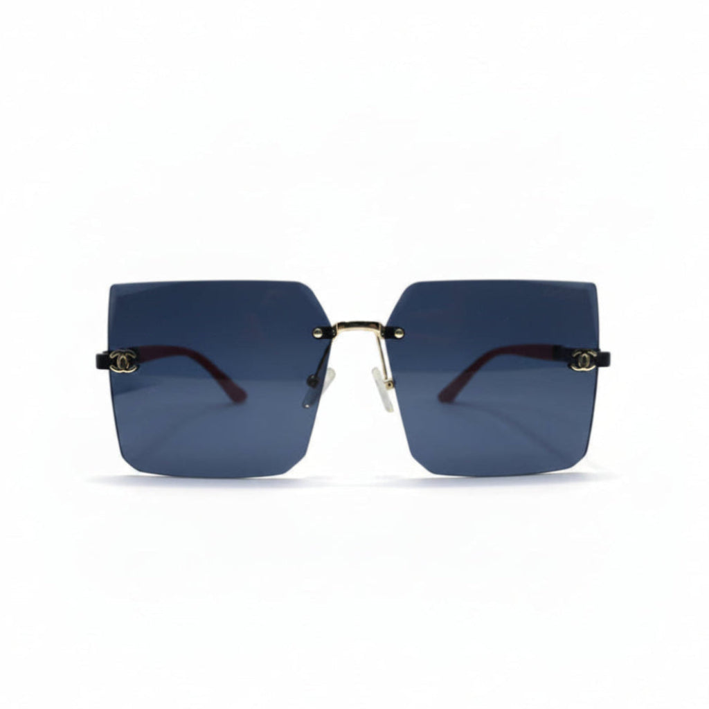 Rimless square sunglasses with dark blue lenses, gold metal frames, and red temple tips, displayed on a white surface with two black textured props on either side.