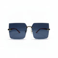 Rimless square sunglasses with dark blue lenses, gold metal frames, and red temple tips, displayed on a white surface with two black textured props on either side.
