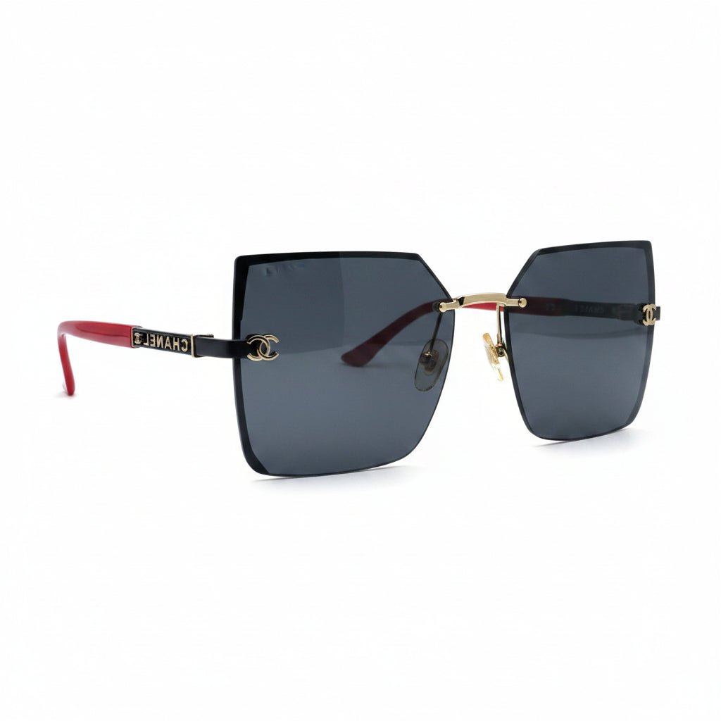 Rimless square sunglasses with dark blue lenses, gold metal frames, and red temple tips, displayed on a white surface with two black textured props on either side.