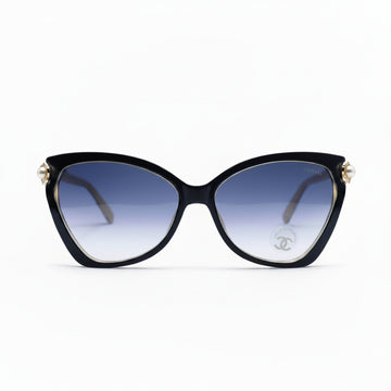Black cat-eye sunglasses with gradient blue lenses and gold-tone metal accents, displayed on a white surface with a soft shadow.