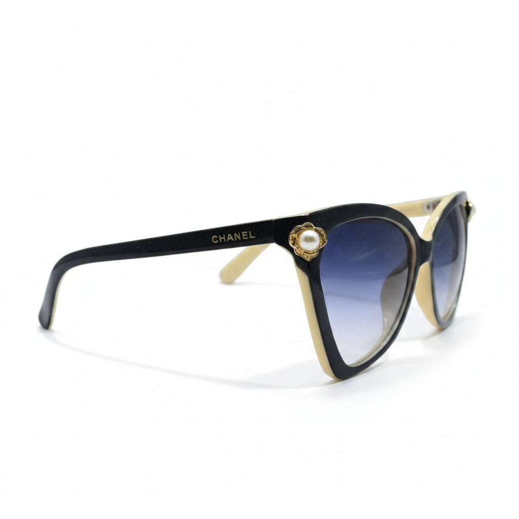Black cat-eye sunglasses with gradient blue lenses and gold-tone metal accents, displayed on a white surface with a soft shadow.