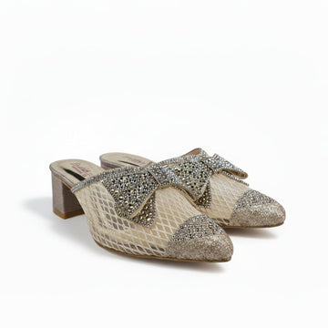 A pair of women's heeled mule sandals with a snakeskin pattern, featuring a large rhinestone-embellished bow on the strap and glittery gold toe caps, set against a plain light gray background.