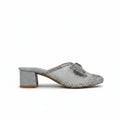 A single women's heeled mule sandal with a silver glittery snakeskin pattern, featuring a textured block heel and a decorative silver bow on the toe strap, set against a light gray background.