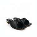 A pair of black leather slide sandals with textured glittery straps and low block heels with gold-toned detailing, photographed on a white fabric background.