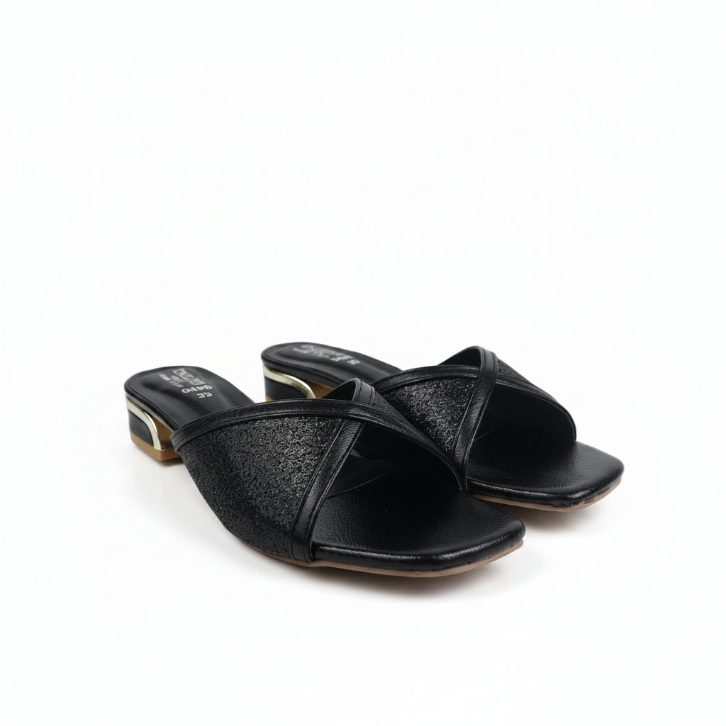 A pair of black leather slide sandals with textured glittery straps and low block heels with gold-toned detailing, photographed on a white fabric background.