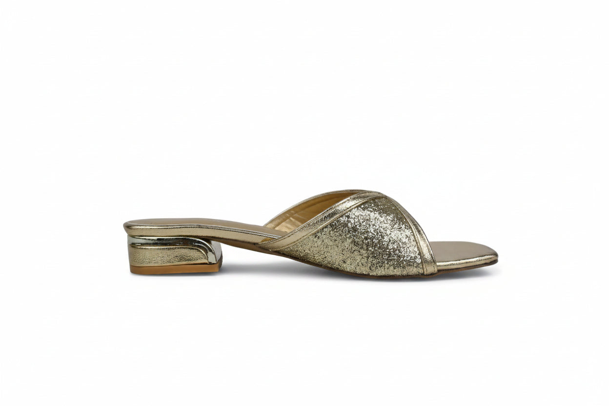 A single metallic gold glitter mule sandal with a low block heel, shown from the side against a light gray fabric backdrop.