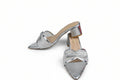 A pair of metallic silver pointed-toe mule heels with a rhinestone-embellished strap and a block heel, shown on a light gray background with a red shoebox partially visible on the right.