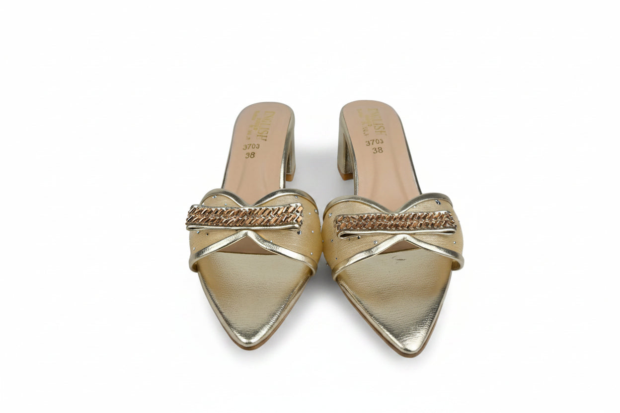 A pair of gold metallic pointed-toe mule heels with a braided chain detail across the instep, photographed on a white fabric background.