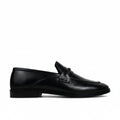 A single black leather penny loafer shown in profile against a light gray fabric backdrop.