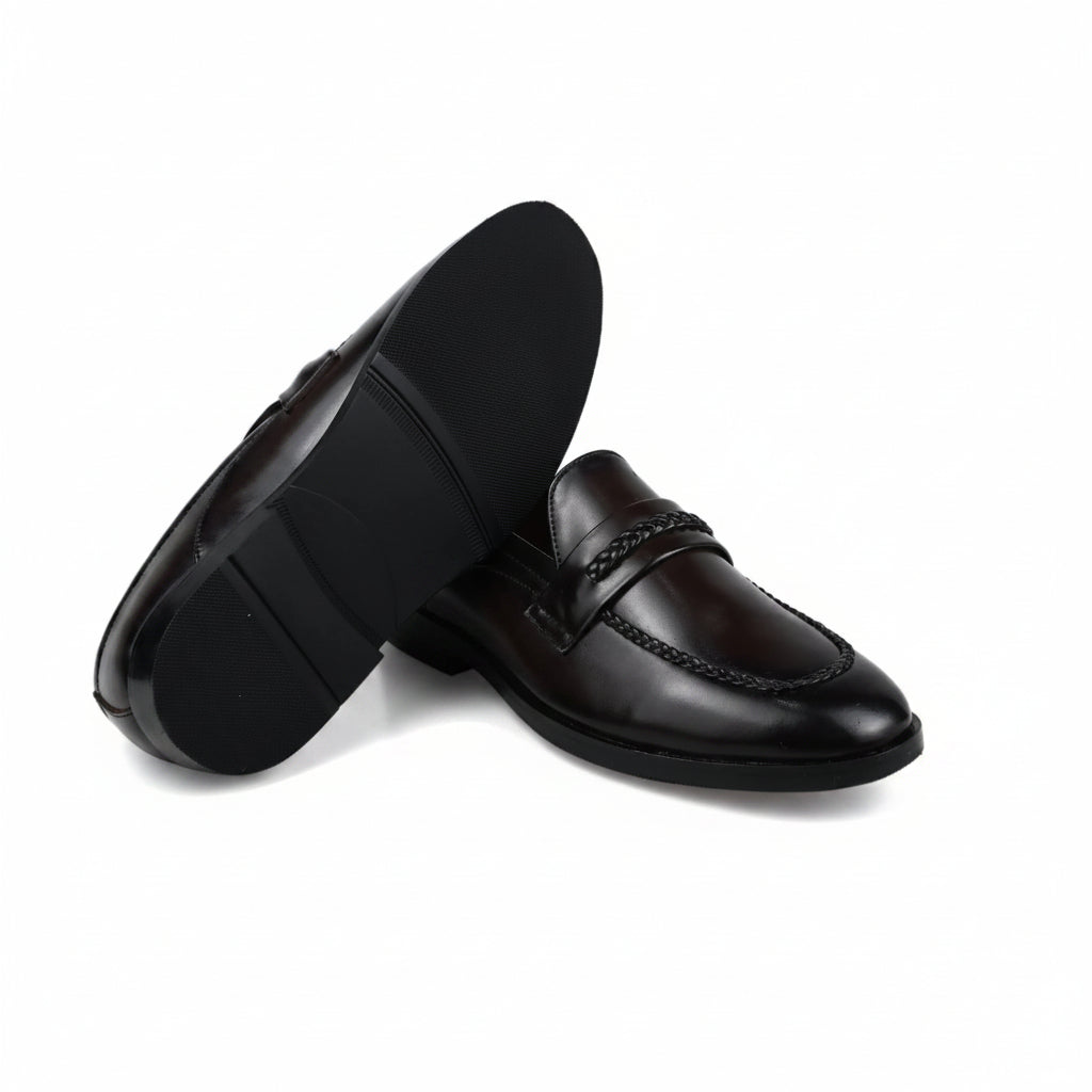 A pair of dark brown leather penny loafers, with one shoe standing upright to show the side and sole, and the other lying on its side to show the toe and vamp. The shoes are photographed on a wrinkled white fabric background.