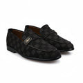 A pair of black checkered loafers with a gold-tone metal logo plaque on the side, displayed on a white fabric background.