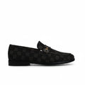A single black checkered loafer with a small gold-tone metal emblem on the vamp, photographed against a wrinkled white studio backdrop.