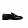 A single dark brown leather penny loafer with a decorative strap and small gold-tone buckle detail, positioned horizontally against a wrinkled white studio backdrop.